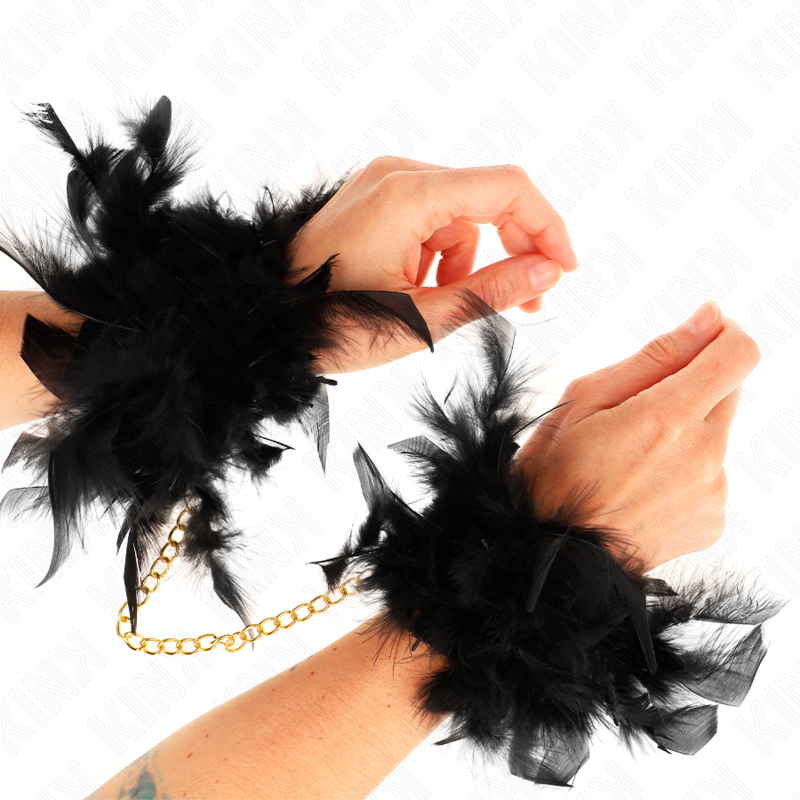 Pair of elegant black feather handcuffs with gold chain, worn on wrists, perfect for adding style and flair to costumes or playful settings.